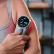 Grå håndholdt laser med rundt farvedisplay, der lyser rødt mod en overarm
