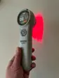 Grå håndholdt Heat Sense Laser PRO 3.0 med rundt display, der lyser rødt på en væg