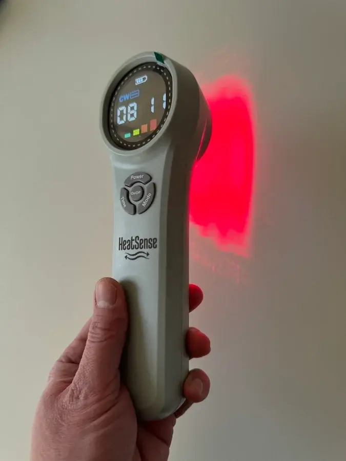Grå håndholdt Heat Sense Laser PRO 3.0 med rundt display, der lyser rødt på en væg