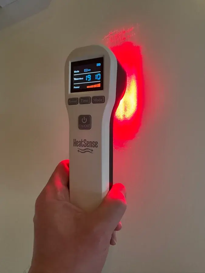 Hvid håndholdt Heat Sense Laser S 2.0 med display, der kaster rødt lys på en væg