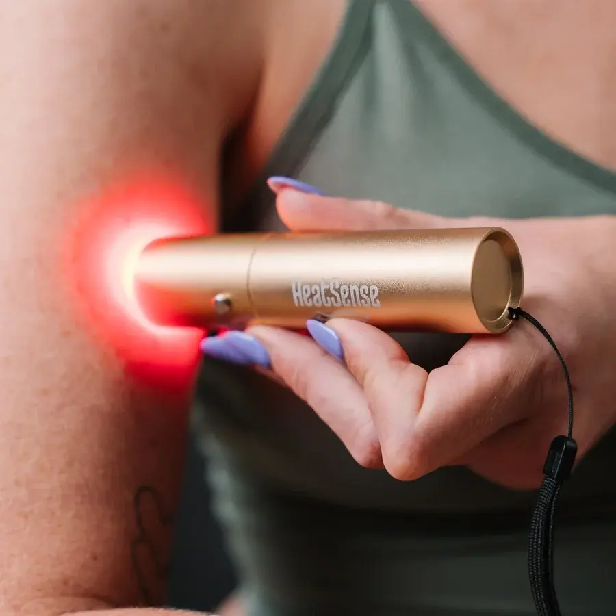 Guldfarvet Heat Sense-lyspen med håndstrop, der lyser rødt mod en overarm