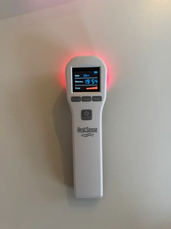 Hvid Heat Sense-laser med tændt display og rødt lys i toppen, fotograferet mod en lys væg